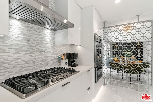 kitchen with wall chimney range hood, stainless steel gas cooktop, white cabinets, a notable chandelier, and decorative backsplash