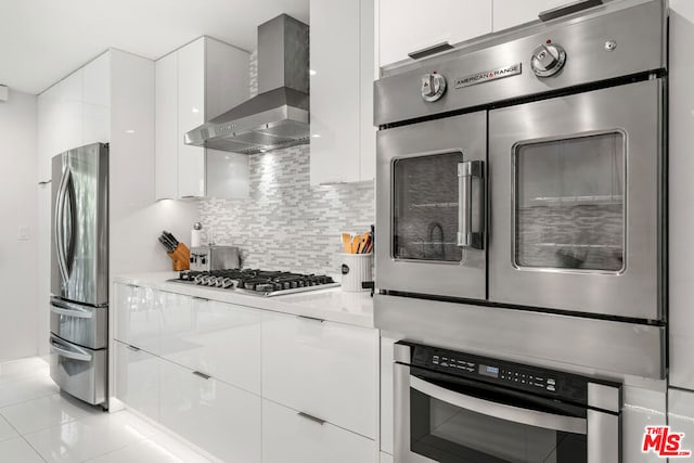 kitchen featuring backsplash, light tile patterned floors, white cabinetry, wall chimney exhaust hood, and stainless steel appliances