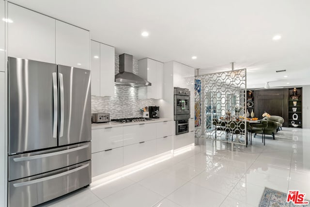 kitchen with hanging light fixtures, white cabinetry, stainless steel appliances, wall chimney exhaust hood, and decorative backsplash