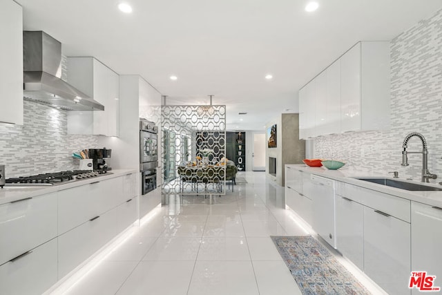 kitchen with white cabinetry, stainless steel appliances, wall chimney range hood, and sink