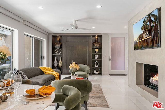 living room with a high end fireplace, ceiling fan, built in shelves, and light tile patterned floors