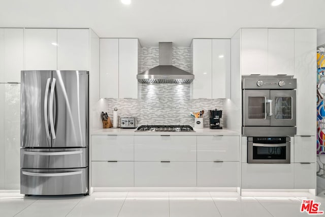 kitchen with decorative backsplash, white cabinets, wall chimney range hood, and stainless steel appliances