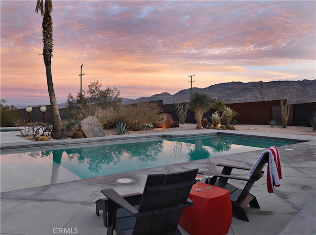 pool at dusk featuring a patio and a mountain view