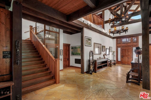 foyer featuring a towering ceiling, beamed ceiling, an inviting chandelier, and wooden ceiling