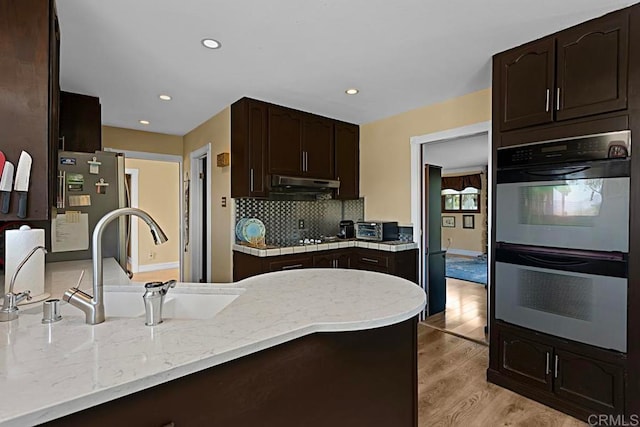 kitchen with tasteful backsplash, sink, double oven, light hardwood / wood-style floors, and stainless steel refrigerator