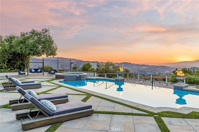 pool at dusk with a patio area, a mountain view, and an in ground hot tub