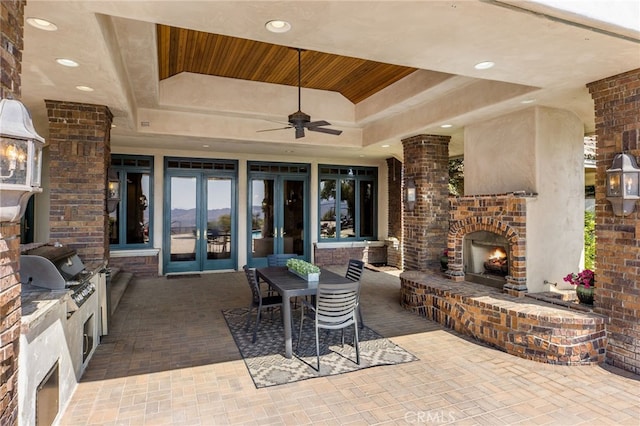 view of patio / terrace featuring an outdoor brick fireplace, french doors, exterior kitchen, ceiling fan, and a grill