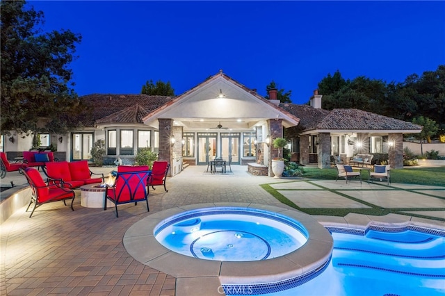 back house at night with french doors, a patio, and a pool with hot tub