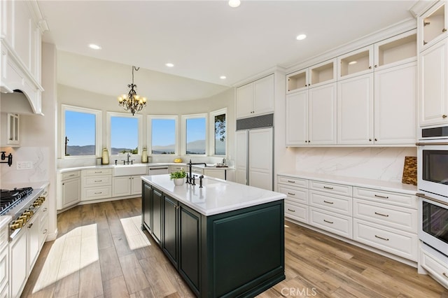 kitchen featuring decorative backsplash, hanging light fixtures, a center island with sink, light hardwood / wood-style floors, and a notable chandelier