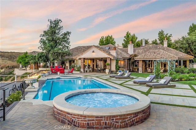 pool at dusk with a patio and an in ground hot tub