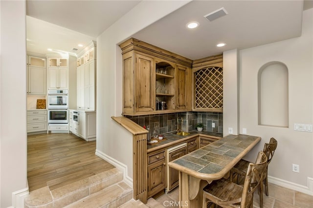 bar featuring light hardwood / wood-style floors, tile countertops, stainless steel double oven, and backsplash