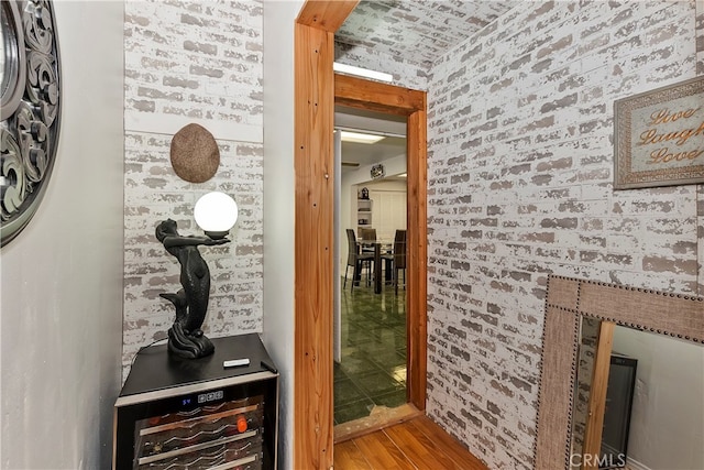 hallway featuring brick wall, wood-type flooring, and beverage cooler