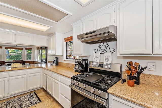 kitchen with light tile patterned floors, light stone countertops, stainless steel gas range, and white cabinets