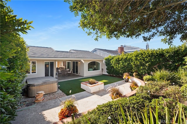 rear view of property featuring a hot tub, a patio, and a lawn