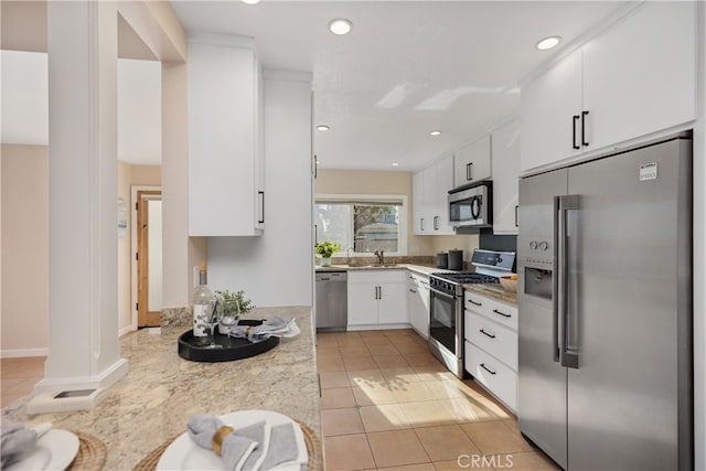 kitchen with sink, stainless steel appliances, white cabinets, light stone counters, and light tile patterned floors