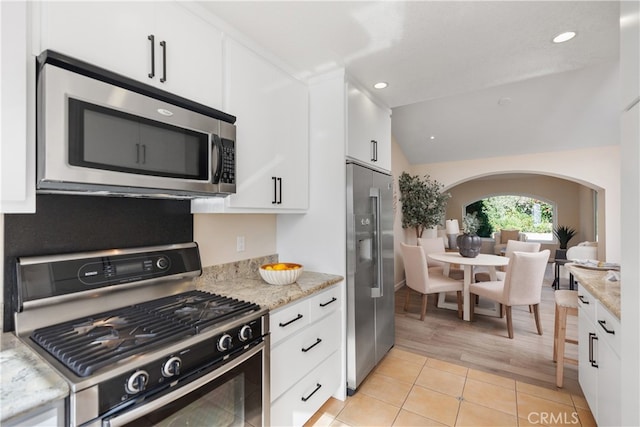 kitchen featuring vaulted ceiling, stainless steel appliances, white cabinetry, and light hardwood / wood-style floors