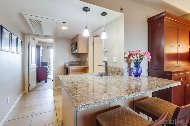 kitchen featuring kitchen peninsula, light tile patterned floors, a kitchen bar, pendant lighting, and sink