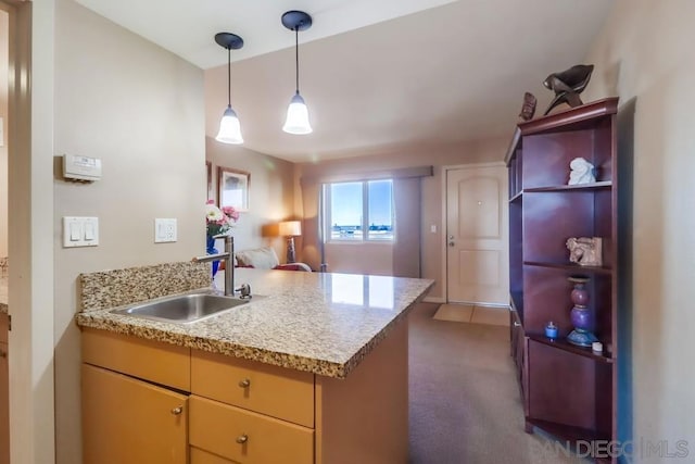 kitchen with light stone countertops, sink, kitchen peninsula, and dark colored carpet