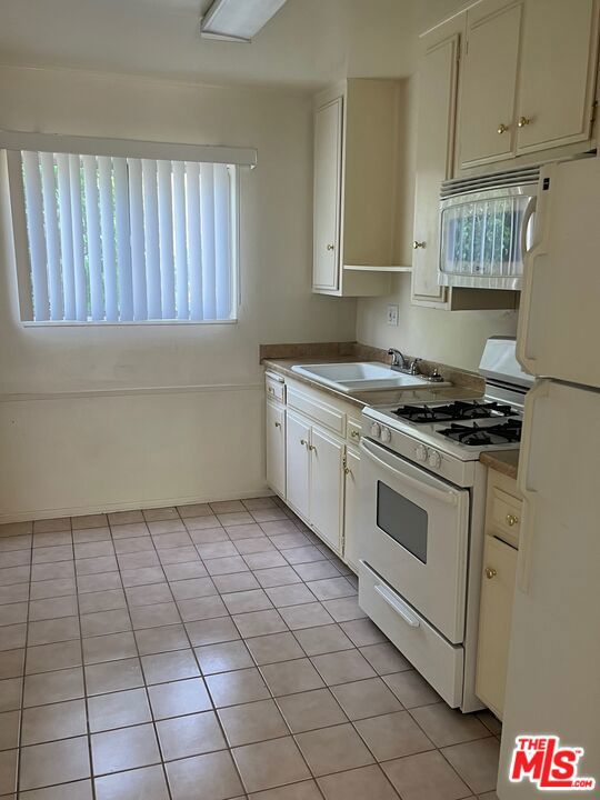 kitchen with light tile patterned flooring, white cabinets, sink, and white appliances