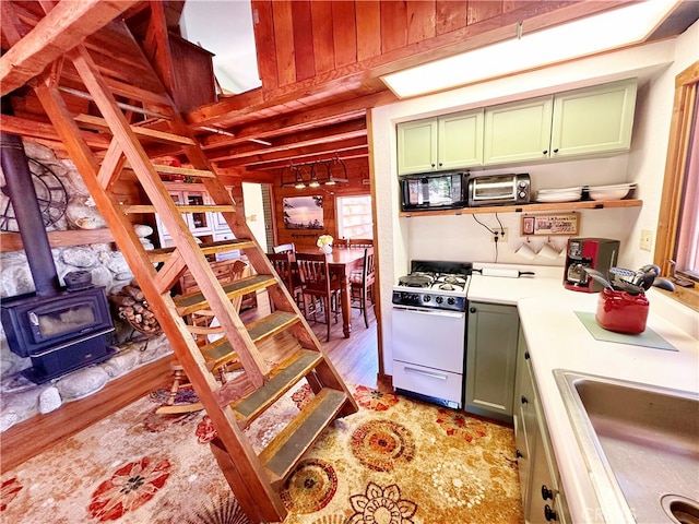 kitchen featuring wooden walls, white gas range oven, a wood stove, green cabinetry, and light hardwood / wood-style floors