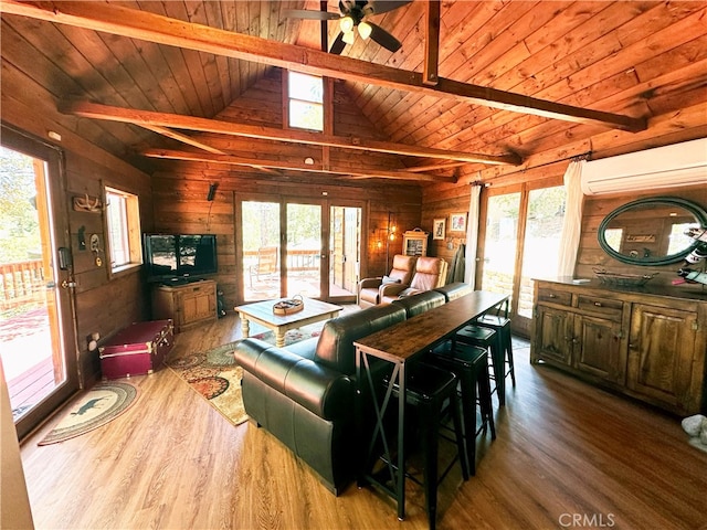 living room featuring a wealth of natural light, an AC wall unit, vaulted ceiling with beams, and wood-type flooring