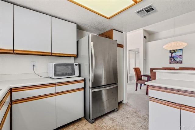 kitchen with decorative light fixtures, white cabinets, stainless steel fridge, and a textured ceiling