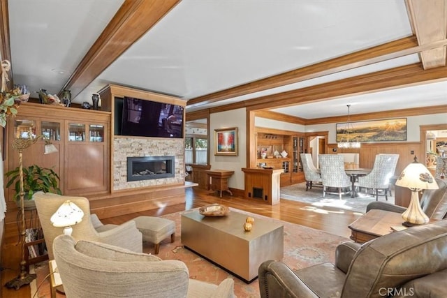 living room with a fireplace, beam ceiling, an inviting chandelier, crown molding, and light wood-type flooring