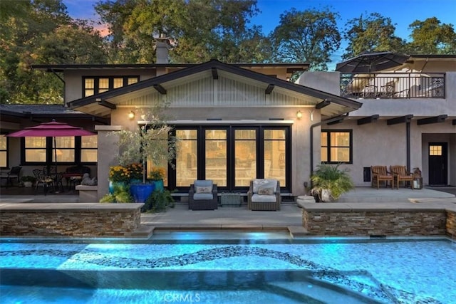 back house at dusk with pool water feature, an outbuilding, a balcony, and a patio