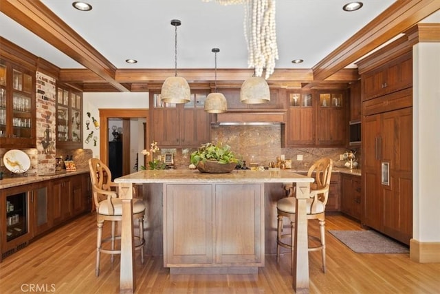 kitchen featuring light hardwood / wood-style floors, beamed ceiling, hanging light fixtures, a breakfast bar area, and light stone counters