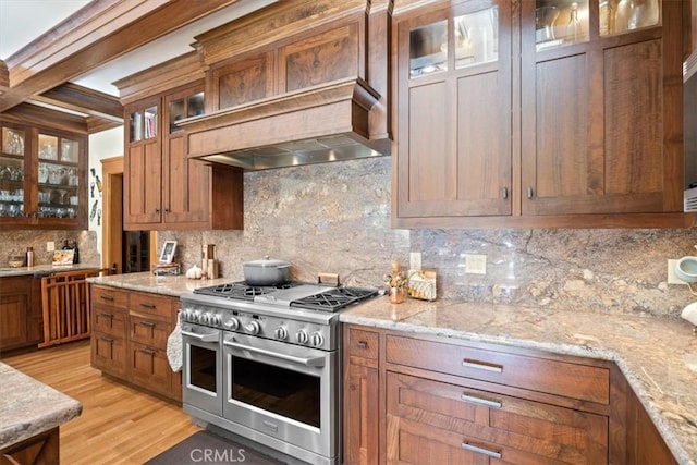 kitchen with backsplash, range with two ovens, beam ceiling, light hardwood / wood-style flooring, and light stone counters