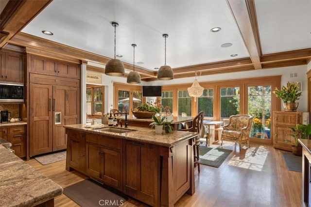 kitchen featuring light stone countertops, pendant lighting, built in appliances, an island with sink, and beam ceiling