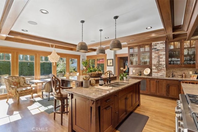 kitchen with high end stainless steel range oven, light hardwood / wood-style floors, a center island with sink, french doors, and sink