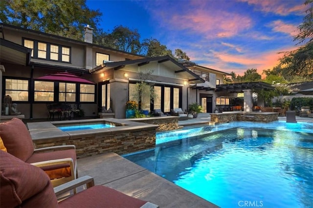 pool at dusk featuring pool water feature, a patio area, and an in ground hot tub