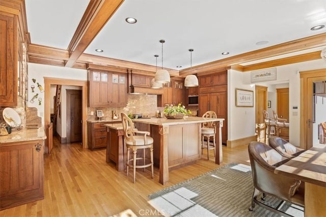 kitchen with a kitchen island, light hardwood / wood-style floors, hanging light fixtures, light stone counters, and a breakfast bar