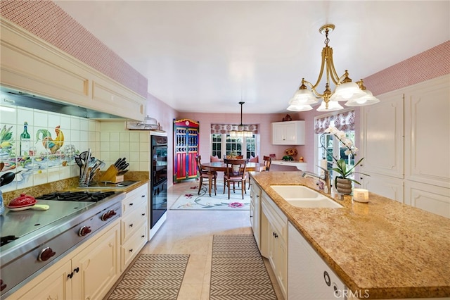 kitchen with an island with sink, a notable chandelier, stainless steel gas cooktop, hanging light fixtures, and sink