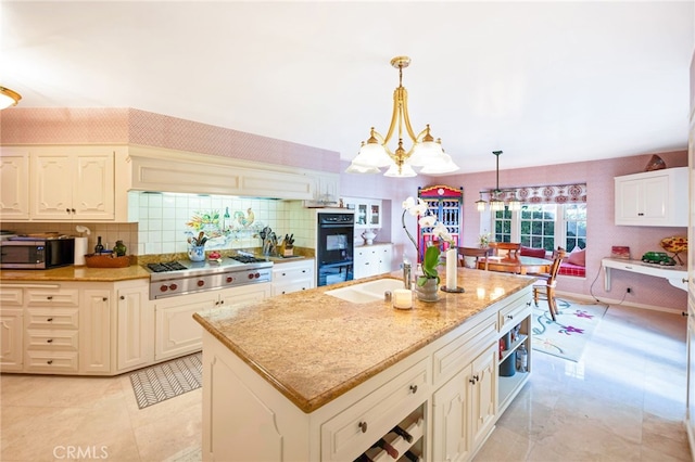 kitchen with an island with sink, stainless steel appliances, a notable chandelier, pendant lighting, and sink