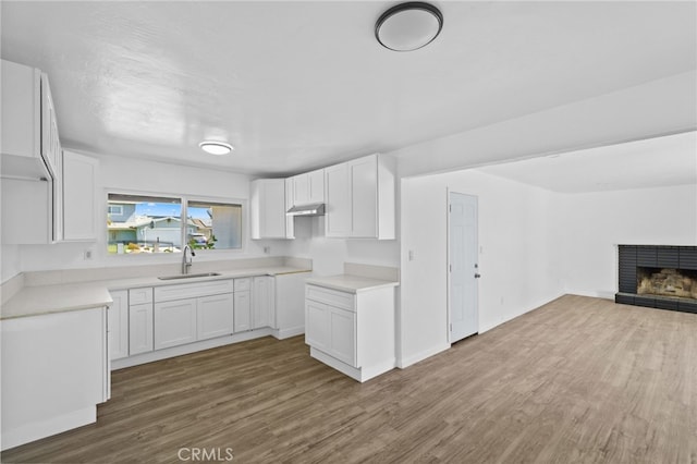 kitchen featuring wood-type flooring, sink, a fireplace, and white cabinets