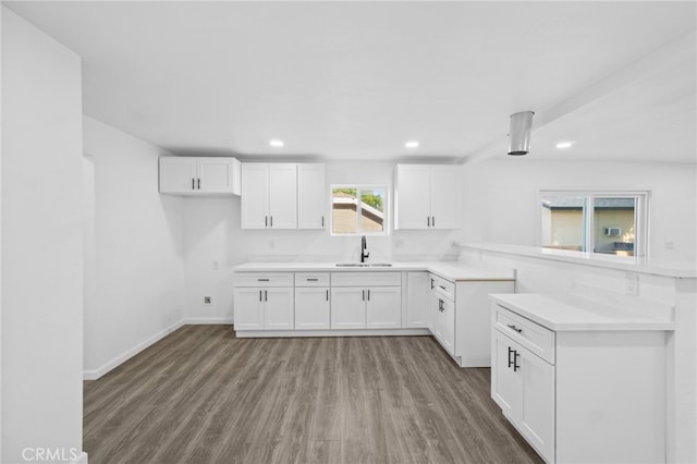 kitchen with kitchen peninsula, white cabinets, sink, and wood-type flooring