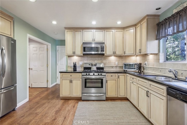 kitchen with light hardwood / wood-style floors, tasteful backsplash, stainless steel appliances, and sink