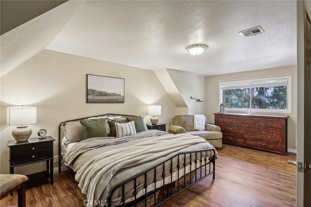 bedroom featuring a textured ceiling, wood-type flooring, and vaulted ceiling