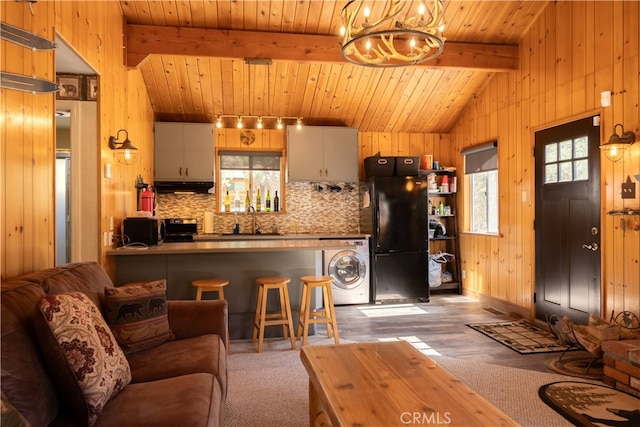 kitchen with washer / dryer, lofted ceiling with beams, black appliances, and wooden walls