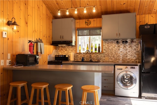 kitchen with washer / clothes dryer, a breakfast bar area, wooden walls, black appliances, and sink