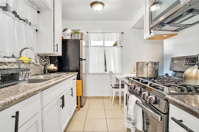 kitchen with decorative backsplash, sink, light tile patterned floors, stainless steel gas range, and white cabinets