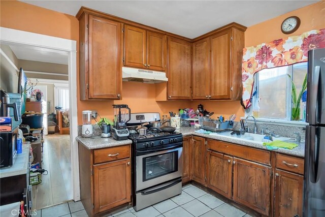 kitchen featuring sink, light tile patterned floors, stainless steel gas range, and black refrigerator