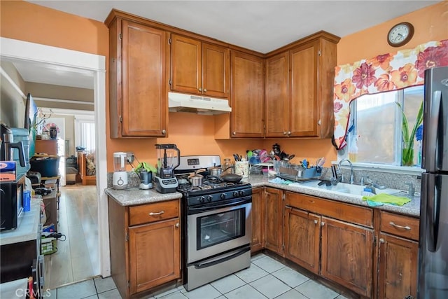 kitchen with sink, light tile patterned floors, stainless steel gas stove, black refrigerator, and light stone counters