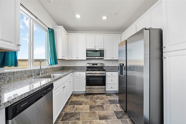 kitchen featuring stone counters, white cabinets, stainless steel appliances, and sink