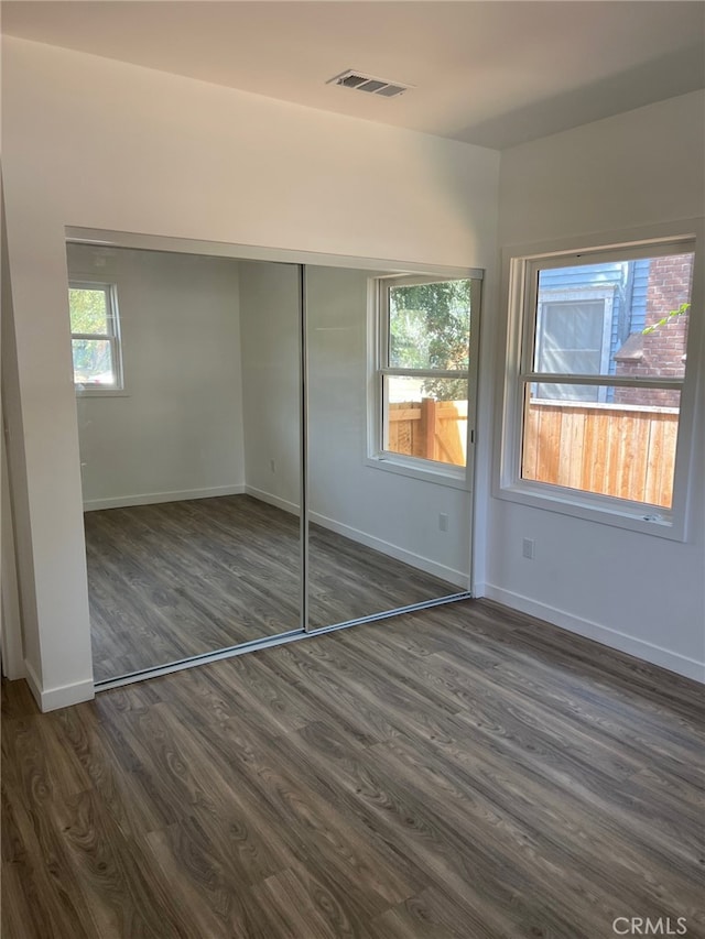 unfurnished bedroom featuring dark hardwood / wood-style flooring, a closet, and multiple windows