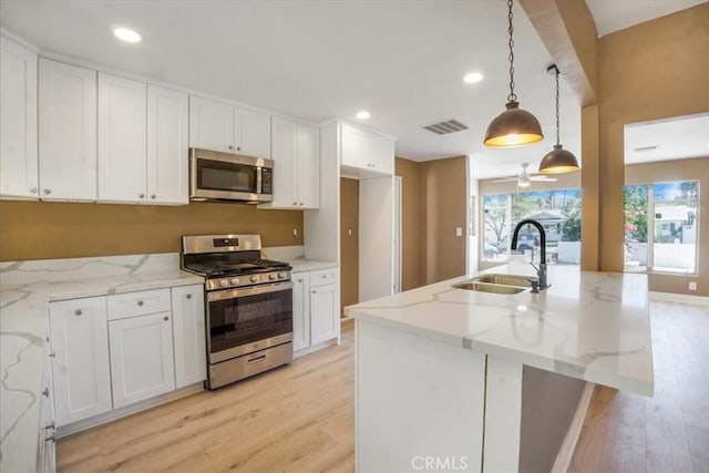 kitchen with light stone countertops, appliances with stainless steel finishes, decorative light fixtures, and sink