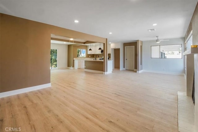 unfurnished living room with ceiling fan, light wood-type flooring, and sink