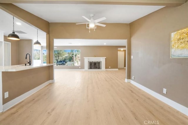 unfurnished living room with ceiling fan, beam ceiling, sink, and light hardwood / wood-style floors